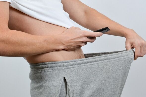 رجل ينظر من أسفل سرواله إلى القضيب المتضخم